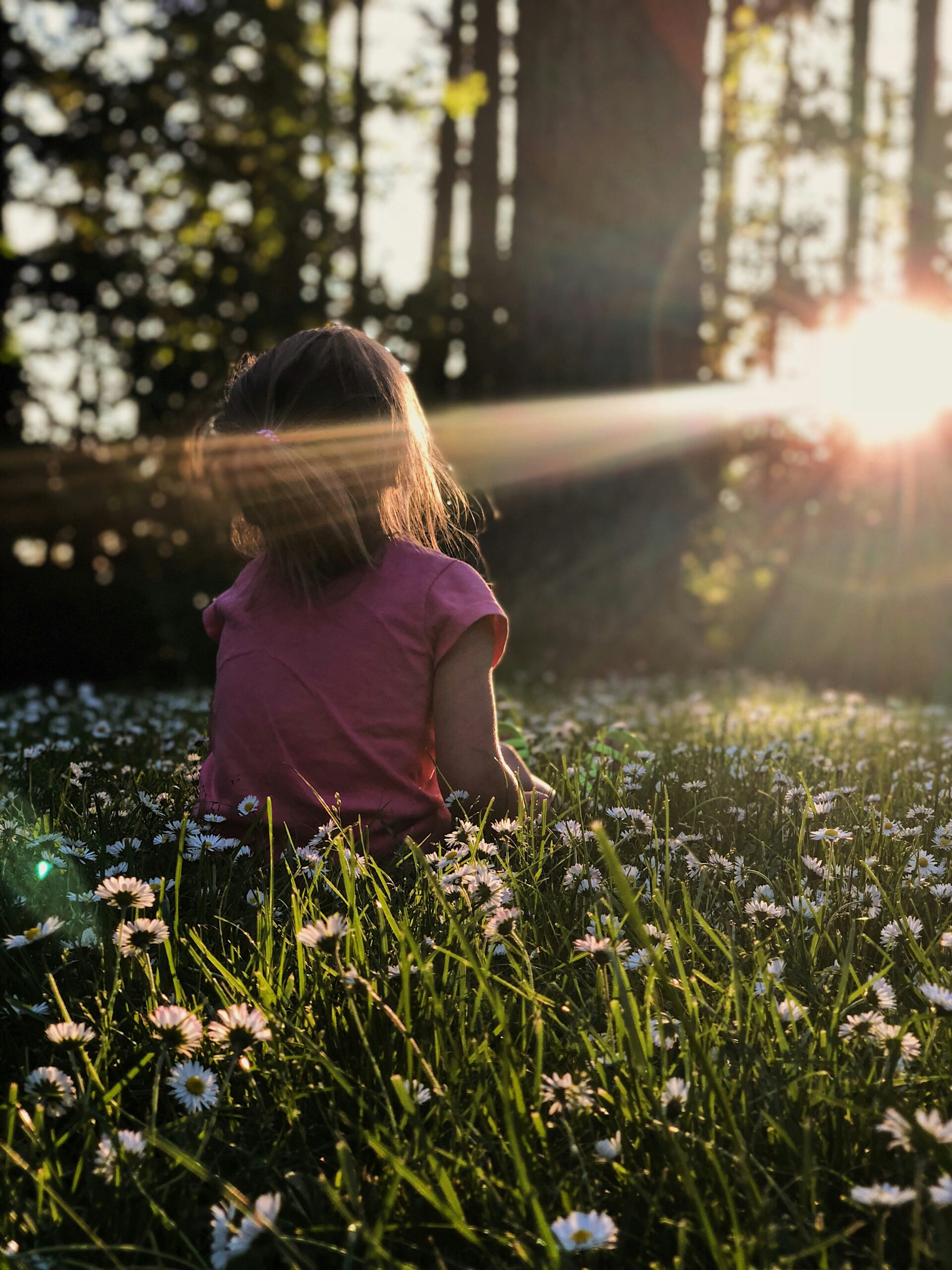 Child sitting barefoot on lush green grass, connecting with the Earth to practice grounding. The image shows a serene outdoor setting with sunlight filtering through the trees, illustrating the calming effect of earthing on stress and anxiety relief.